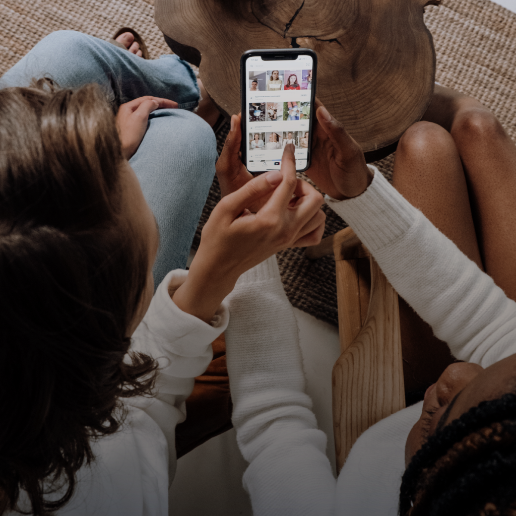 Dos personas sentadas revisan el contenido en un teléfono móvil, enfocándose en una galería de imágenes en la pantalla.