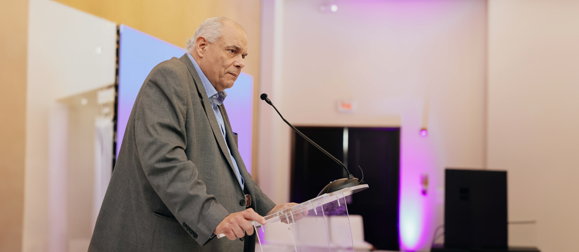 La imagen muestra a una persona en un podio, hablando en un entorno formal, lo que sugiere un discurso o presentación en un evento importante. La iluminación suave en tonos púrpura y la vestimenta formal del orador refuerzan el ambiente profesional y solemne. Esta imagen puede estar relacionada con temas de economía, políticas públicas o iniciativas gubernamentales enfocadas en el apoyo y reactivación de las micro y pequeñas empresas (MYPE).