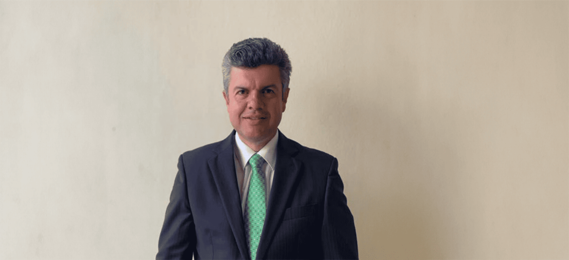 La imagen muestra a un hombre vestido formalmente, de pie contra un fondo claro. Su postura es firme y profesional, transmitiendo una imagen de seriedad y confianza, posiblemente en un contexto relacionado con estrategias de desarrollo empresarial o propuestas de la OIT para fomentar.