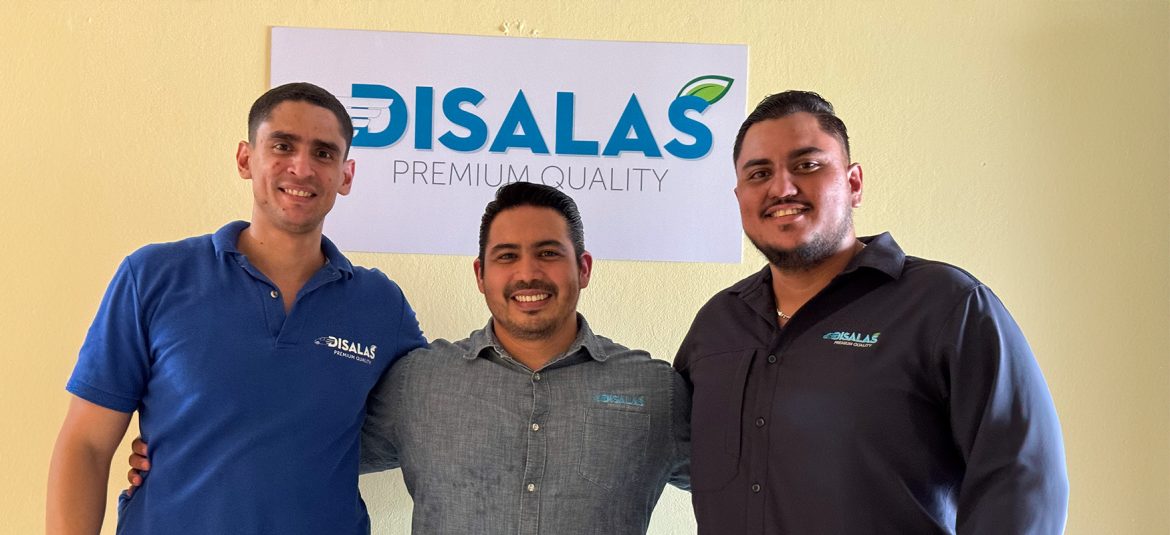 Tres hombres posan juntos frente a un letrero en la pared que dice "DISALAS Premium Quality." Están vestidos con camisas de la empresa, sonriendo y mostrando un ambiente de compañerismo y profesionalismo. La imagen representa una reunión de equipo o socios en un entorno de trabajo dedicado a la calidad en su industria.