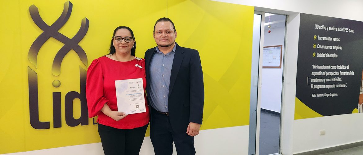 Una mujer y un hombre posando juntos en frente de un muro amarillo con el logo de LID, mientras la mujer sostiene su diploma de graduación. La mujer lleva una blusa roja con una cinta blanca, mientras que el hombre viste un traje oscuro y camisa azul. En el fondo, se puede ver una cita motivacional relacionada con el programa de formación de la Escuela LID de FUSAI.