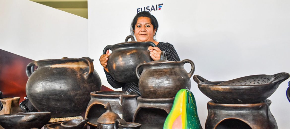 Mujer emprendedora muestra orgullosa sus artesanías de barro negro, incluyendo ollas, comales y hornillas, en una exposición organizada por FUSAI.