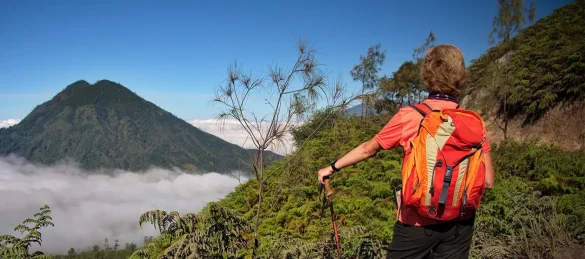 Persona con mochila observa paisaje montañoso desde sendero natural, reflejando turismo sostenible y oportunidades para microempresas en destinos emergentes de El Salvador.