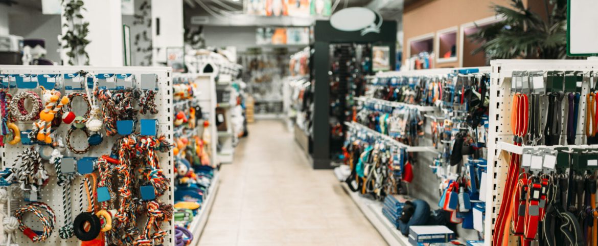 Pasillo interior de una tienda de productos para mascotas, con estanterías a ambos lados repletas de juguetes de cuerda, correas, collares y accesorios en variedad de colores.