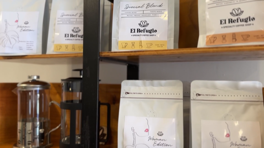Estantería de cafetería artesanal que exhibe bolsas de café de especialidad de la marca “El Refugio”, entre ellas la edición “Special Blend” y “Woman Edition”. En los estantes también se observan cafeteras tipo prensa francesa y utensilios para preparación de café. La escena muestra un ambiente cálido y ordenado, enfocado en productos locales de calidad.
