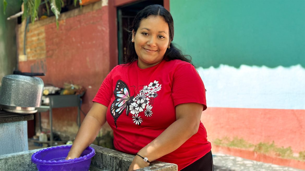 Mujer emprendedora salvadoreña sonríe mientras realiza tareas del hogar, representando el trabajo invisible que muchas empresarias MYPE realizan diariamente.