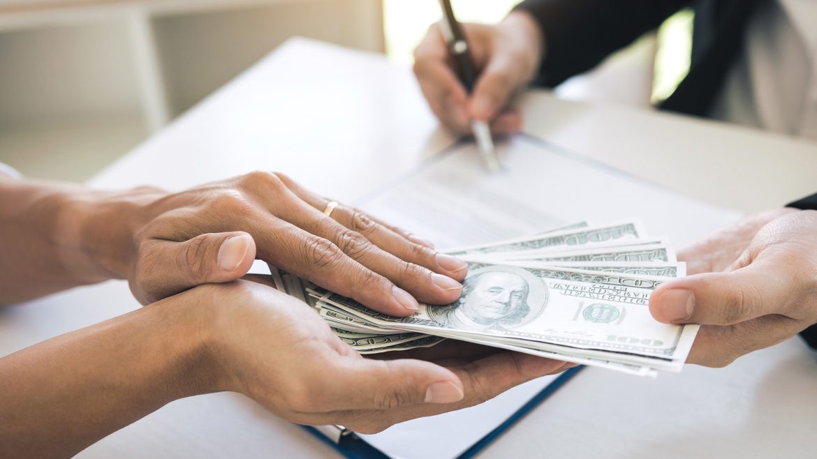 Persona recibiendo dinero en efectivo mientras firma un documento de préstamo, ilustrando temas de financiamiento, crédito y prevención del sobreendeudamiento en El Salvador.