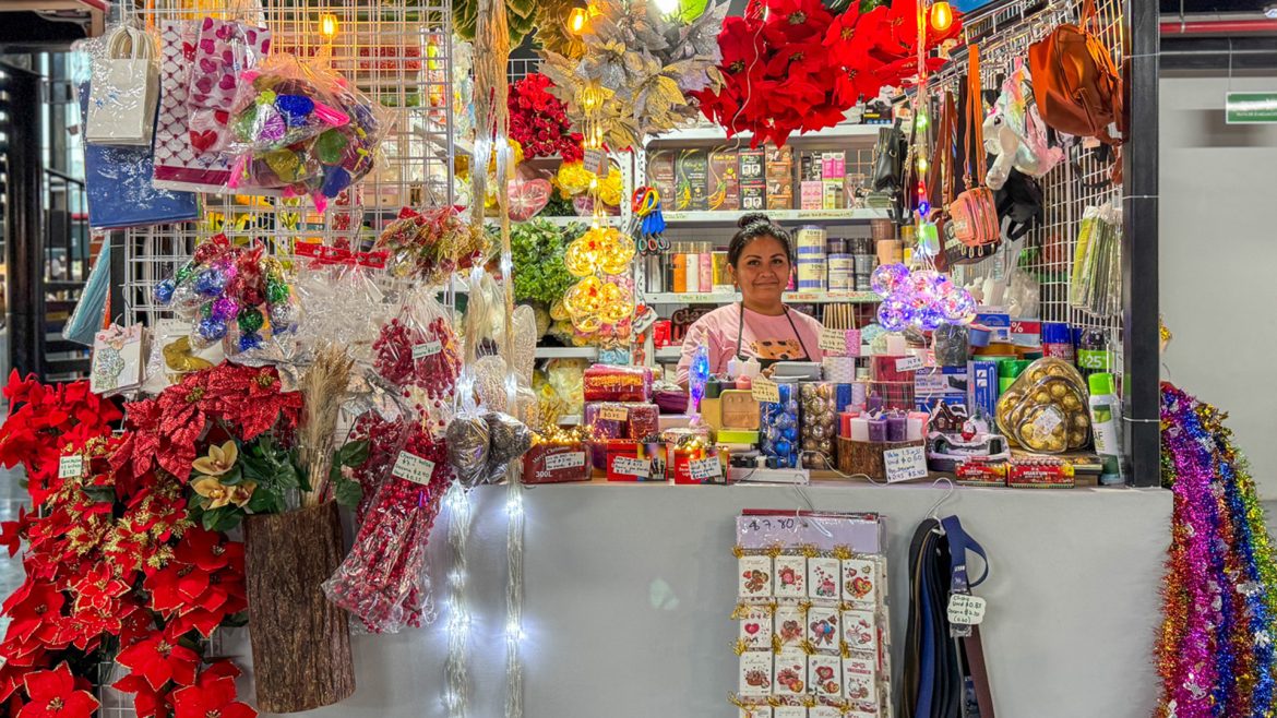 Emprendedora atendiendo un colorido puesto con decoraciones navideñas y artículos variados, representando la actividad comercial de las MYPE durante la temporada alta de ventas.