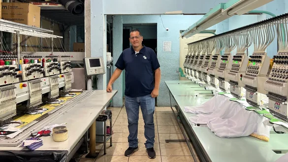 Empresario en taller de bordado industrial junto a maquinaria textil, reflejando productividad y crecimiento de mipymes manufactureras