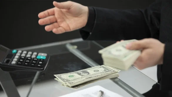 Persona cuenta billetes junto a calculadora en mostrador, reflejando endeudamiento y riesgos financieros para mipymes en El Salvador