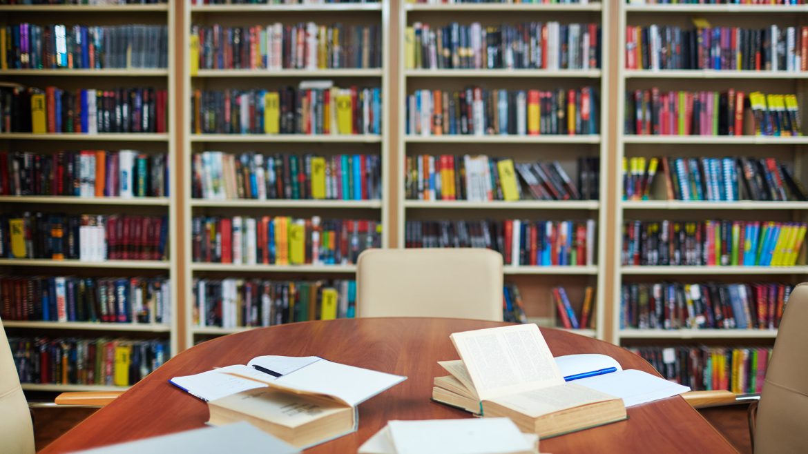 Mesa de lectura en una biblioteca rodeada de estanterías llenas de libros, símbolo de la industria editorial y el conocimiento