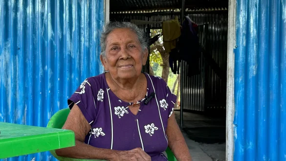 Mujer adulta mayor sentada frente a su vivienda, reflejando servicios de cuidado y bienestar social en comunidades y mipymes locales