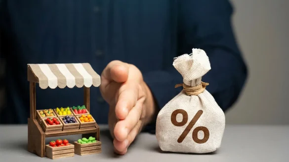 Mano protege maqueta de negocio y saco con símbolo %, representando inclusión financiera y acceso a crédito para mipymes en El Salvador