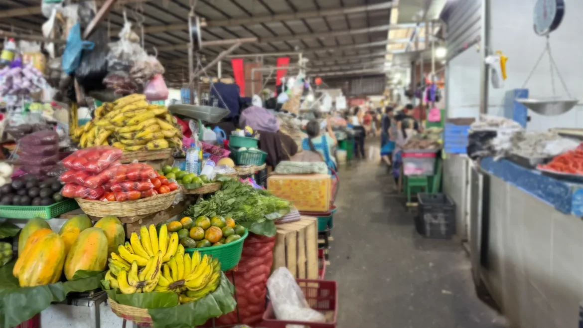 Puesto de mercado con frutas y verduras frescas como plátanos, papayas, tomates y cítricos, en un mercado tradicional concurrido
