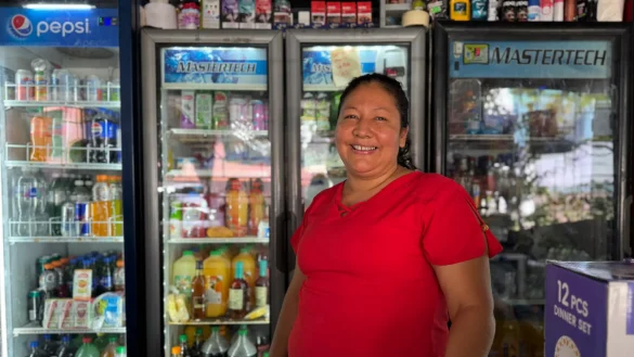 Mujer atiende tienda de colonia frente a refrigeradores con bebidas, reflejando comercio local y acceso limitado a financiamiento en mipymes