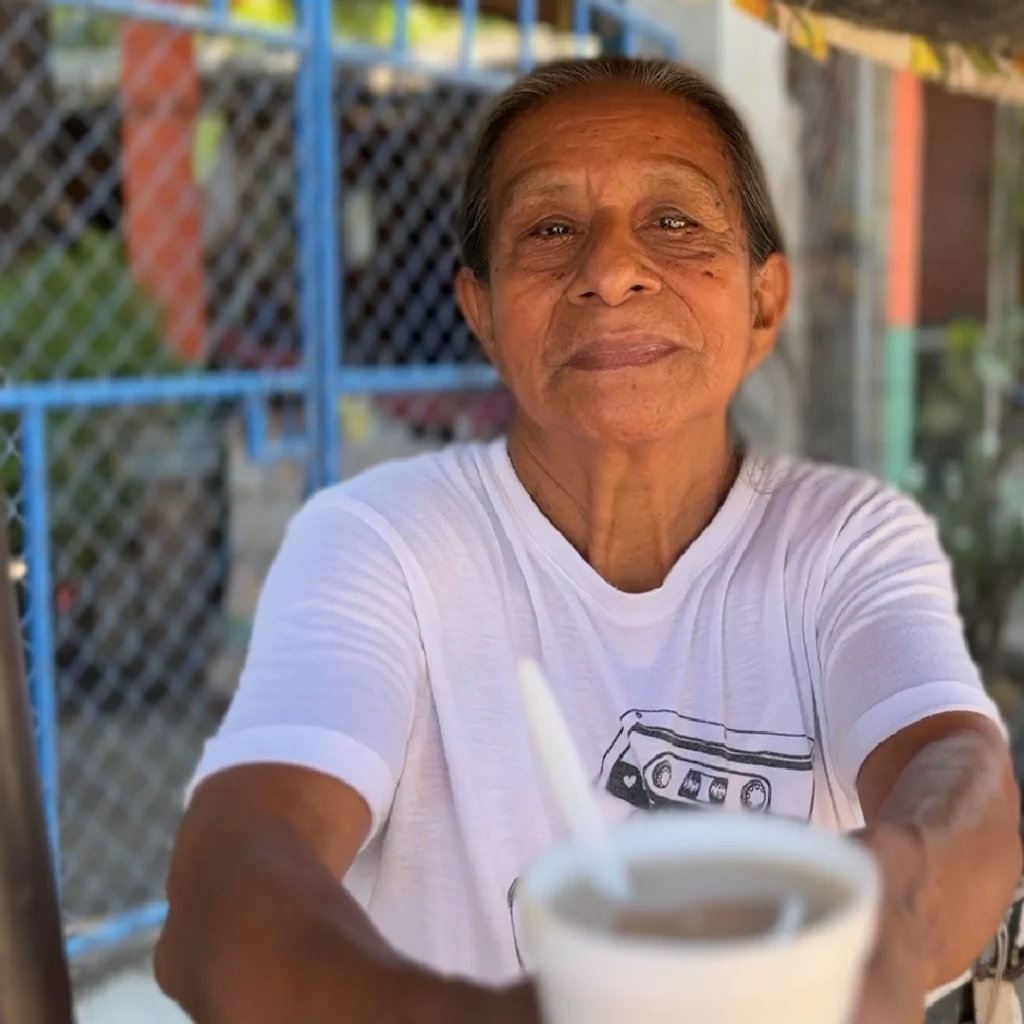 Mujer emprendedora mayor sirve bebida en su negocio local en El Salvador, reflejando autoempleo y economía informal en mipymes rurales